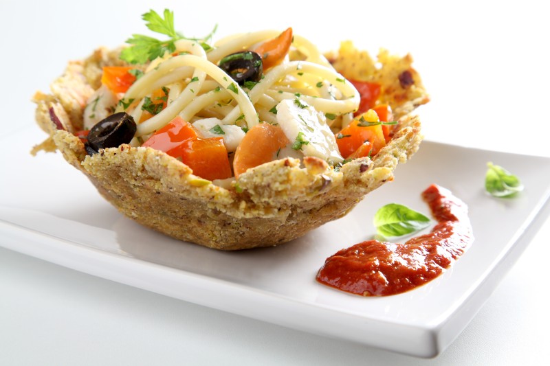 Perciati pasta with strips of peppers, amberjack, sea scallops and black olives in a bread and pistachio basket